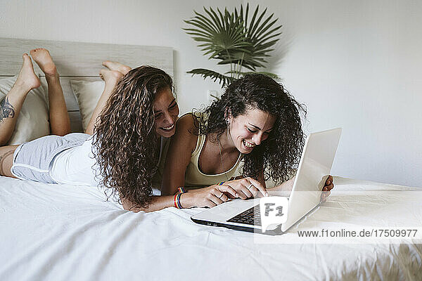 Glückliches lesbisches junges Paar benutzt Laptop  während es zu Hause im Bett liegt