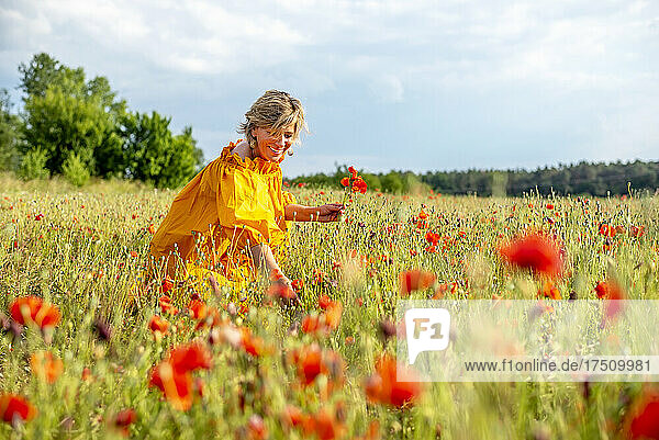 Glückliche reife Frau pflückt Mohnblumen auf dem Feld vor dem Himmel