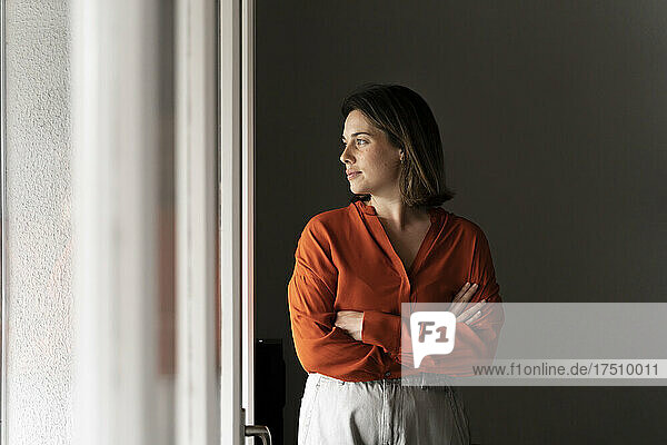 Businesswoman with arms crossed looking through window at home