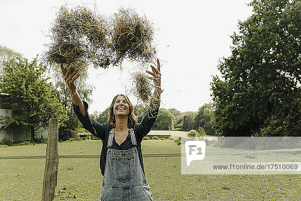Happy young woman in the countryside throwing up hay