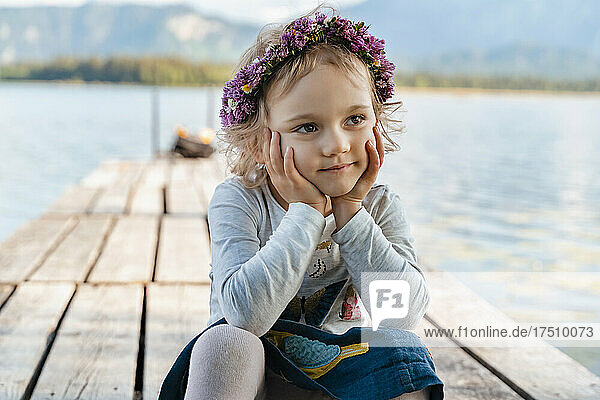 Nahaufnahme eines süßen Mädchens mit Tiara  das auf einem Steg am See sitzt
