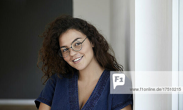 Smiling woman with eyeglasses leaning on wall