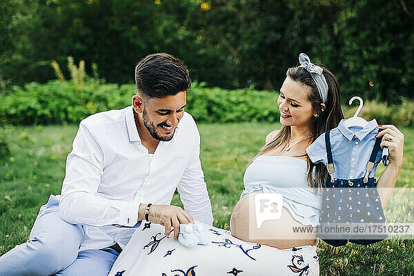 Happy expectant couple with baby booties and clothes spending leisure time in park