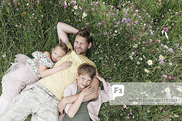 Lächelnder Vater mit Kindern  die auf dem Land inmitten von Blumen liegen