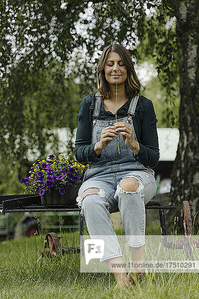 Young woman sitting next to flower box holding grass stalk