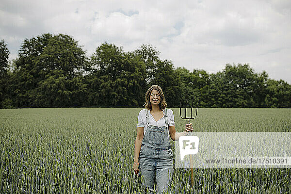 Junge Frau mit Heugabel steht auf einem Getreidefeld auf dem Land