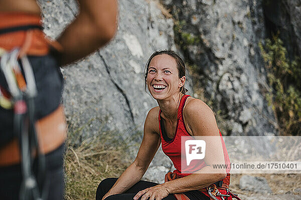Cheerful female climber looking at friend while relaxing on mountain