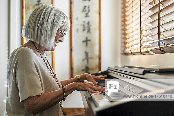 Lächelnde ältere Frau mit Sonnenbrille  die zu Hause Klavier spielt