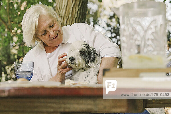 Smiling senior woman playing with dog while sitting at table in yard