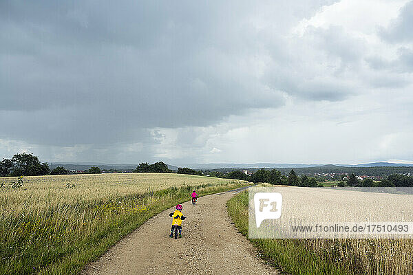 Mädchen mit Fahrrad und Laufrad auf Feldweg  Regenwolken