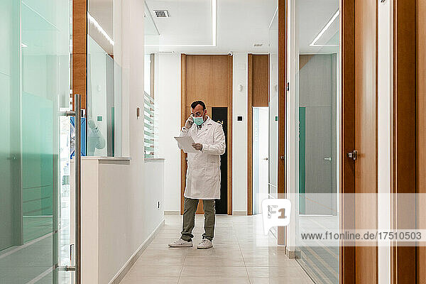 Zahnarzt liest Akte  während er im Flur des Krankenhauses telefoniert