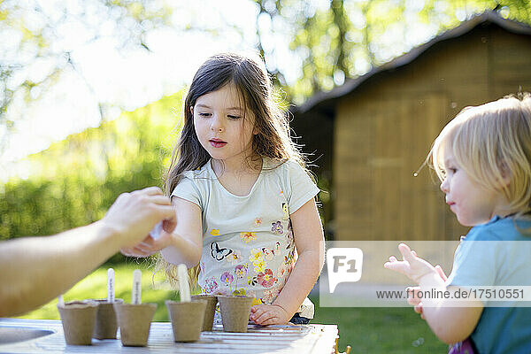 Father giving seeds to girl while gardening on table at yard