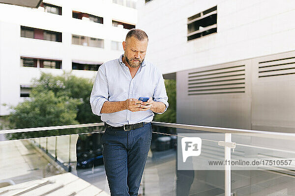 Geschäftsmann benutzt Smartphone  während er auf dem Bürobalkon steht