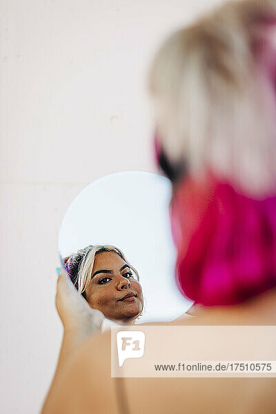 Woman looking her reflection in hand mirror