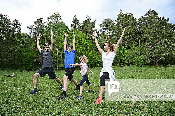 Family practicing warrior poses on grassy land in forest