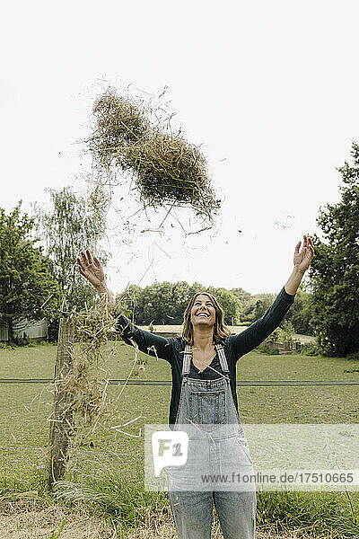 Happy young woman in the countryside throwing up hay