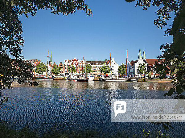 Germany  Schleswig-Holstein  Lubeck  Boats moored along bank of Trave with buildings of Travemunde in background