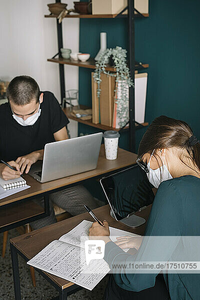 Young man and woman wearing protective masks working on desks at home