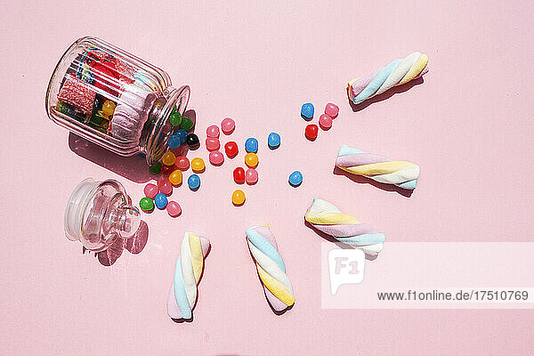 Studio shot of twisted marshmallows and candies spilling out from toppled jar