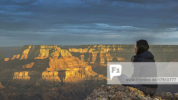 USA  Arizona  Rückansicht einer Frau  die bei Sonnenuntergang auf einem Felsen am Grand Canyon sitzt