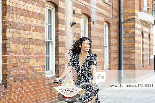 Smiling beautiful woman riding bicycle against building in city