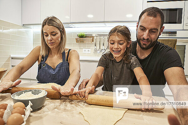 Glückliche Familie knetet Pizzateig mit Nudelholz auf dem Tisch in der Küche