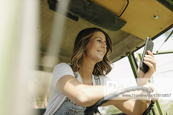 Smiling young woman using mobile phone in a tractor