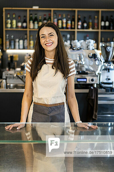 Happy female owner standing at counter in coffee shop