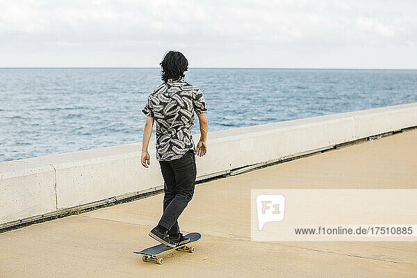 Young man skateboarding on promenade by sea in city