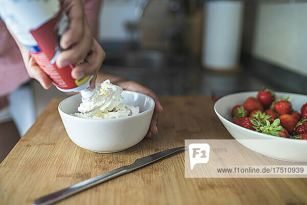 Close-up of young woman adding whipped cream in bowl on cutting board