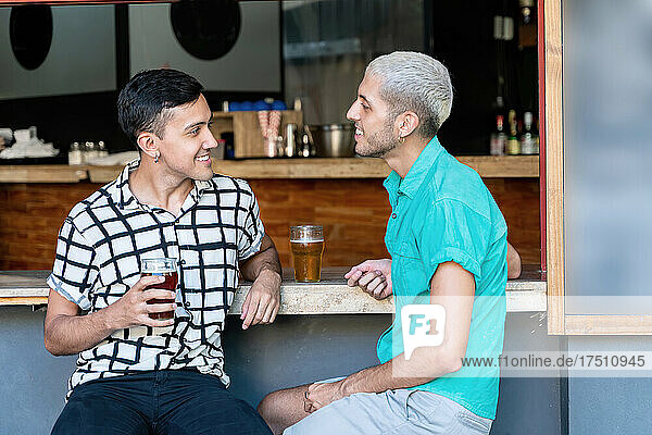 Smiling gay couple talking while drinking beer at bar counter