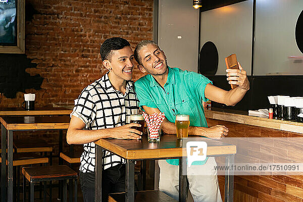 Junges schwules Paar macht Selfie  während es in der Bar Bier trinkt