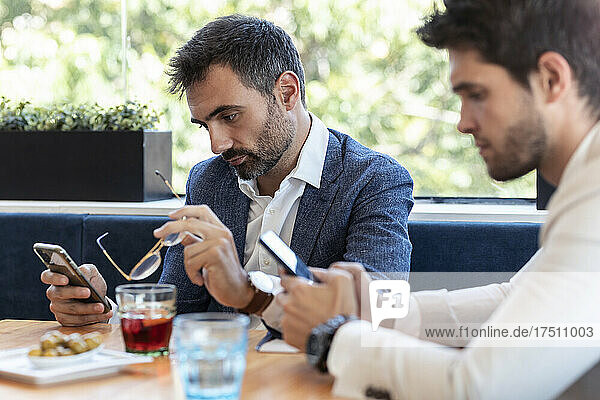 Male coworkers using smart phones in restaurant