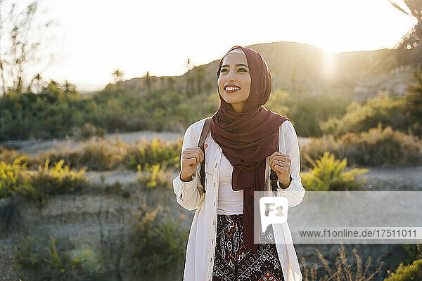 Smiling young tourist woman wearing Hijab in desert landscape looking around