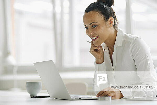 Smiling businesswoman using laptop on desk in home office