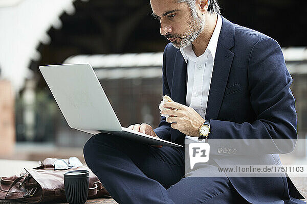 Businessman using laptop while eating food in city