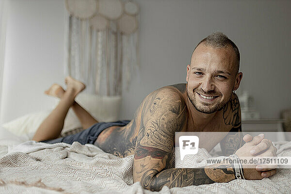Handsome man with tattoo on arm lying on bed