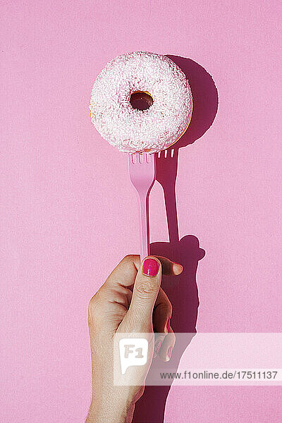 Hand of woman holding fork with sweet doughnut
