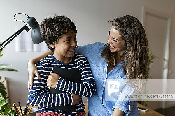 Lächelnde Nachhilfelehrerin und Junge schauen einander an  während sie im Zimmer sitzen