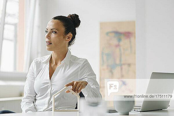 Nachdenkliche Geschäftsfrau mit Musterhaus am Schreibtisch im Heimbüro