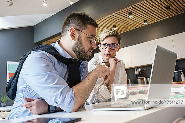 Confident male and female professionals planning strategy while discussing over laptop in office