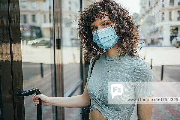 Brunette curly woman wearing protective mask in city