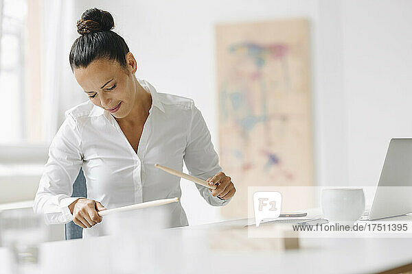 Businesswoman playing on desk with drumsticks while sitting in home office