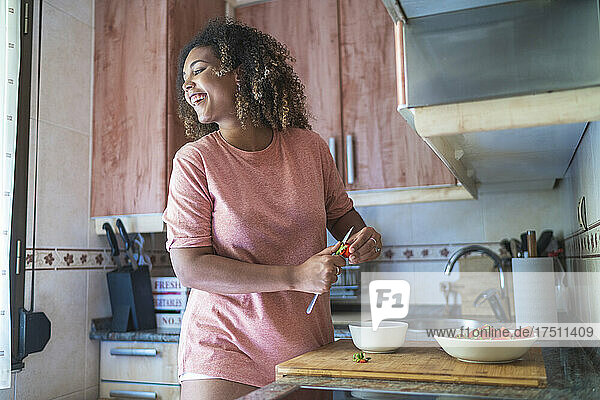 Cheerful young woman looking away while chopping strawberries on kitchen counter at home