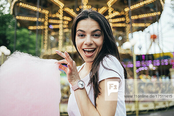 Close-up of beautiful woman holding cotton candy against carousel in amusement park