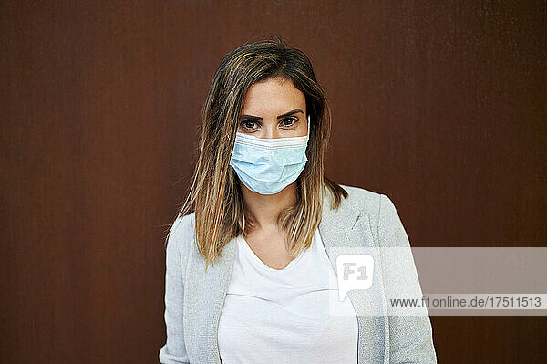 Businesswoman wearing face mask against brown wall
