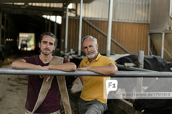 Portrait of mature farmer with adult son at cow house on a farm