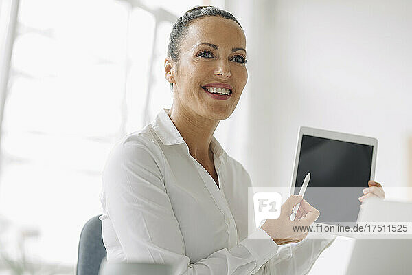 Close-up of smiling entrepreneur holding digital tablet looking away in home office
