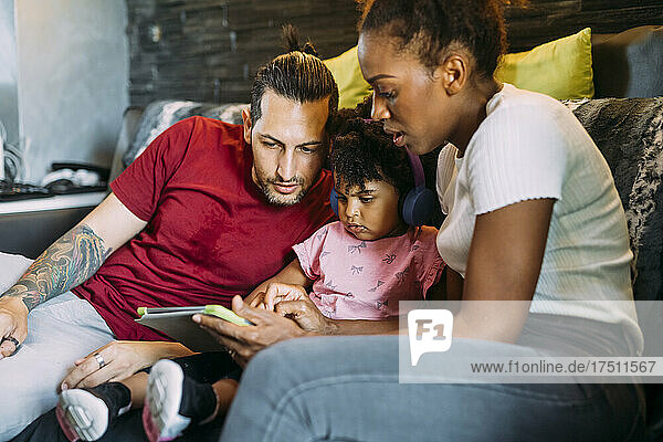 Eltern mit ihrer Tochter nutzen ein digitales Tablet  während sie sich zu Hause auf dem Sofa entspannen