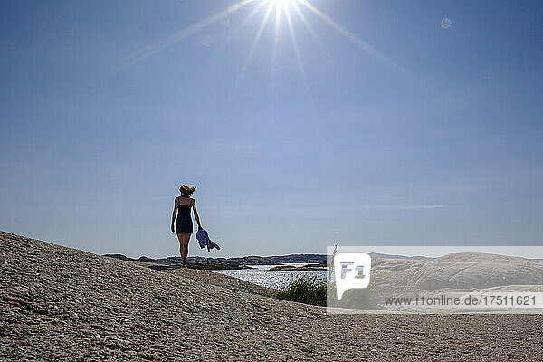 Sun shining over teenage girl walking alone along rocky shore